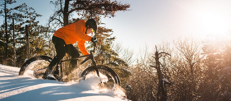 meilleur-fat-bike-electrique-hiver Un homme sur un fat bike roulant dans la neige poudreuse