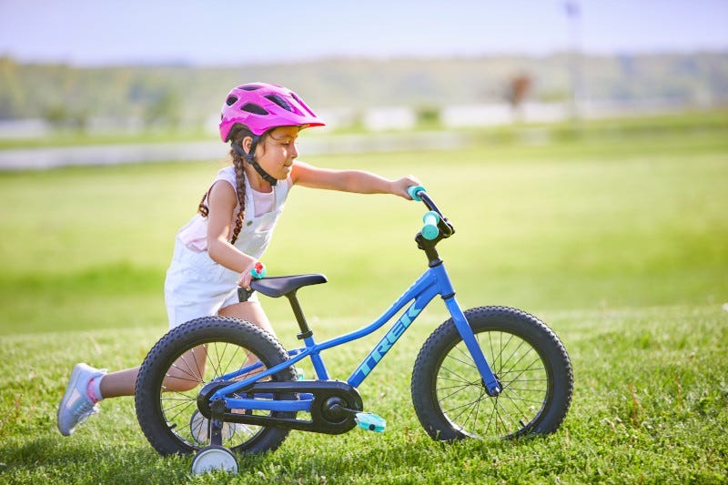 Petite fille poussant un vélo pour enfant 16 pouces avec roues d'entraînement dans l'herbe