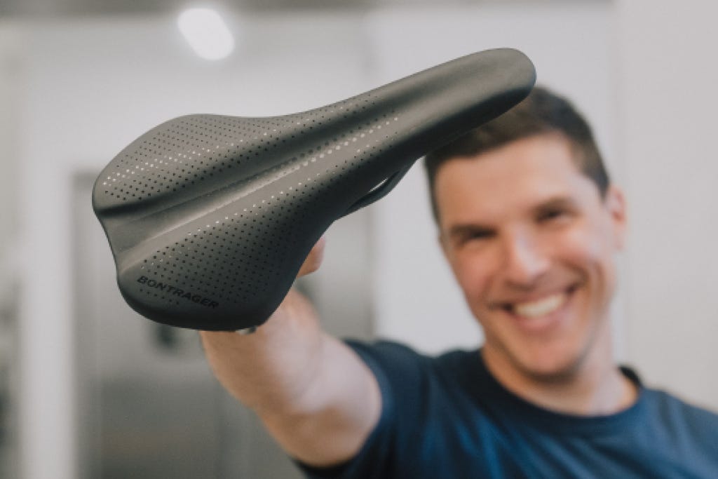 Un homme souriant montre à la caméra une selle de vélo